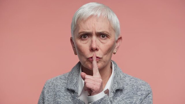 Senior Woman Making Quiet Shush Gesture on Pink