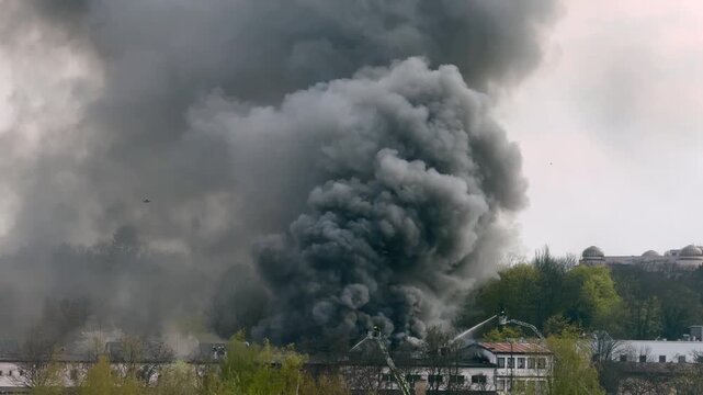 Firefighters battling large fire with flames and thick black smoke in Prague, Europe. Emergency response scene with rescue services controlling burning building and heavy smoke cloud in urban area.