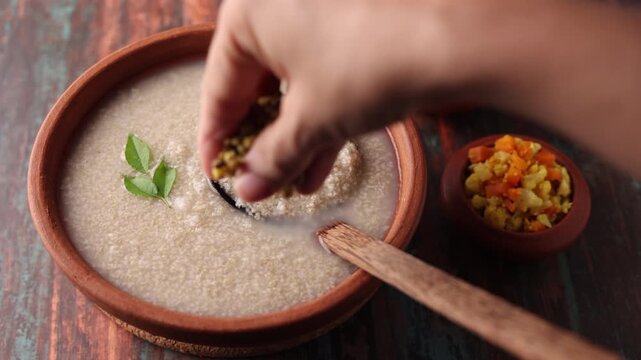 Millet porridge in a mud plate on a wooden table. Millet porridge with lentils healthy breakfast or dinner. Diabetes friendly meal. Kanji fox tail millet in Kerala India.
