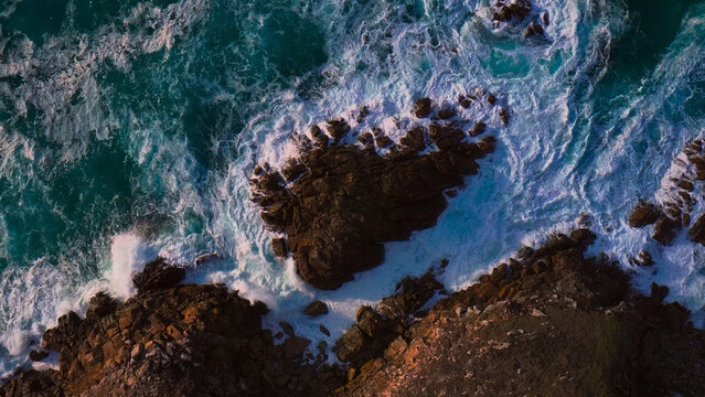 Dramatic aerial view of powerful ocean waves crashing against rugged coastal rocks, a vibrant turquoise and white sea creating a dynamic natural backdrop
