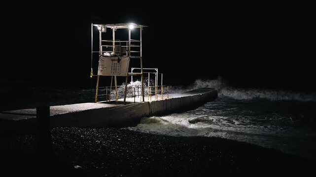 There is a lifeguard's cabin on the night beach. Waves are visible next to the breakwater.