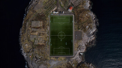 Remote island soccer field, a dramatic aerial view of a green football pitch surrounded by rugged coastal landscape and dark ocean waters, showcasing isolated sports infrastructure. © Shanza
