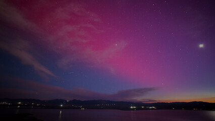 Fototapeta premium Vibrant night sky with stunning purple and pink aurora borealis, tranquil lake reflecting the colorful celestial display, serene twilight landscape for nature and travel themes