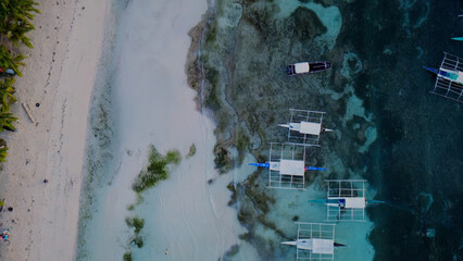 Tropical island paradise, aerial view of white sand beach and turquoise ocean, traditional Filipino outrigger boats anchored in clear shallow water, serene summer vacation destination. © Shanza