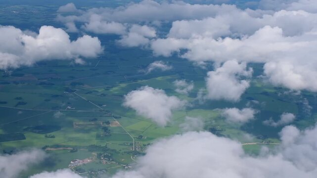 Aerial view from airplane of green meadows. White cumulus clouds in blue sky. Travel, freedom concept. Aviation, transportation