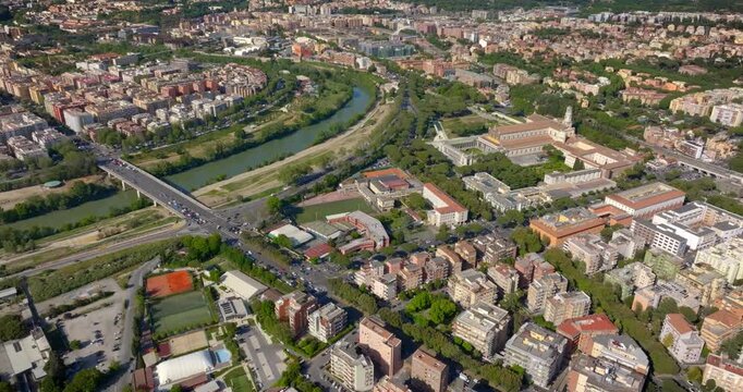 Aerial panorama of Rome, Italy, featuring the Tiber River, Marconi Bridge, and the Basilica of Saint Paul Outside the Walls amidst a dense urban layout with green spaces and residential buildings.
