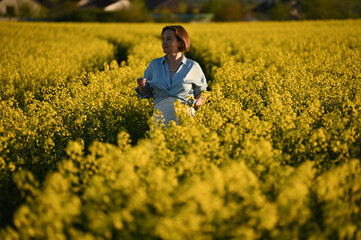 Fototapeta premium Happy smiling woman with hat in yellow rapeseed field at sunset