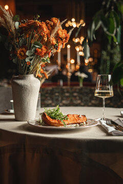 Roasted pumpkin dish with greens on beautifully set restaurant table with flowers candles and wine glass in warm evening light