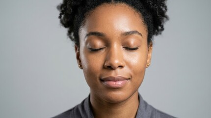 Obraz premium Close-up of a young African American woman’s face with smooth skin and closed eyes, expressing calm, relaxation and wellness on a neutral gray background, soft studio light, realistic skin detail,