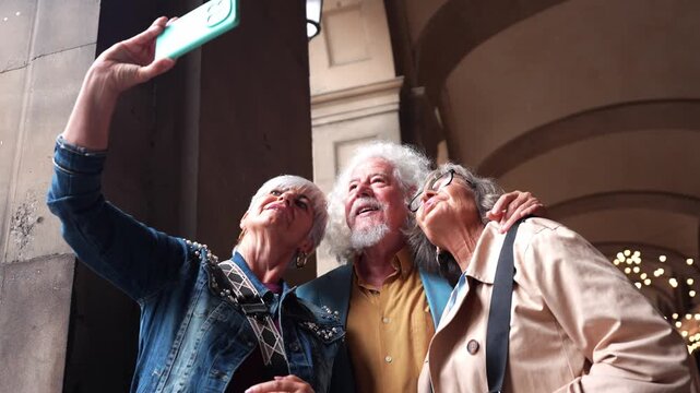 Joyful group of stylish senior friends traveling and taking a selfie with a smartphone, smiling and laughing together in an old city