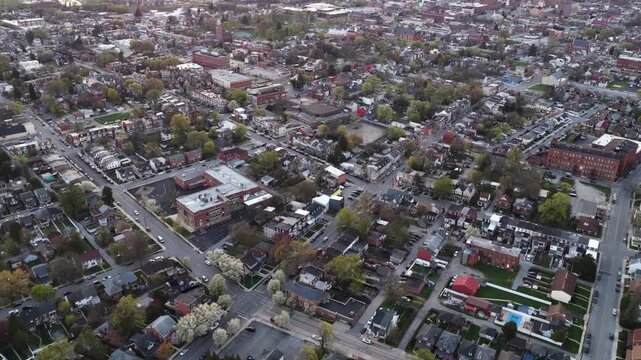 Aerial flyover of historic American town at dusk in spring, showing colorful rooftops, neighborhood streets and classic brick buildings with blooming trees across urban landscape.