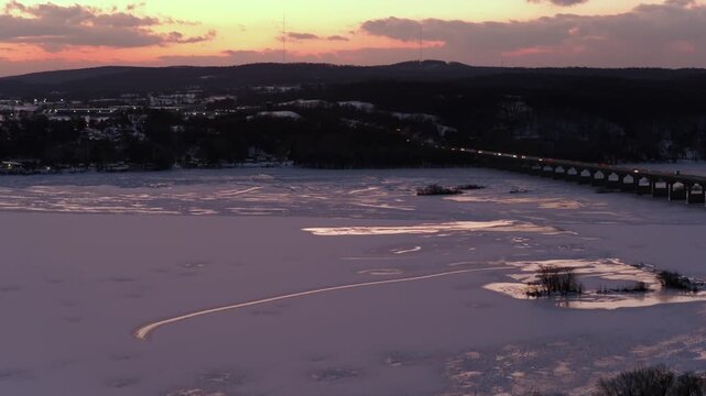 Aerial sunset view of frozen Susquehanna River between Columbia and Wrightsville, Pennsylvania, with bridge traffic, icy water and rolling hills under colorful winter sky. Christmas seson. Panorama.