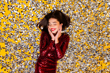 Naklejka premium Woman in red sequin dress lying in silver confetti celebrating with joyful smile and festive glamour