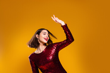 Naklejka premium Confident woman in red sequin dress dancing and smiling against a yellow background, glamorous party portrait conveying joy, energy and festive style