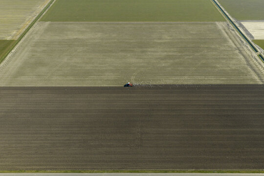Aerial view of a tractor plowing a large agricultural field with a flock of birds following behind in a rural landscape.