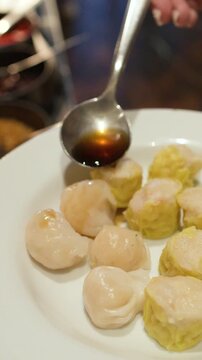 Person Pouring Soy Sauce Over Steamed Shumai and Har Gow Dumplings