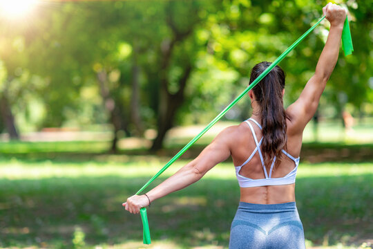 Woman doing shoulder stretch with resistance band band in park performing shoulder mobility