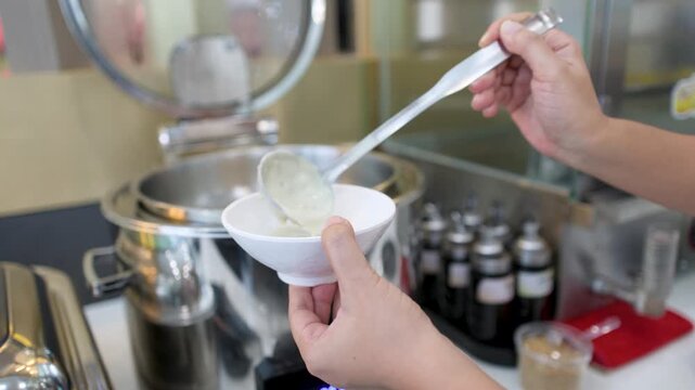 Person Serving Hot Rice Porridge Into a White Bowl at Buffet