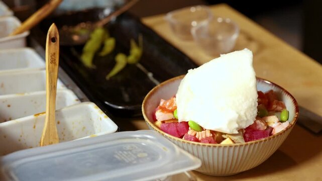 Chef Adding a Large Scoop of White Meringue to a Fresh Poke Bowl