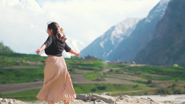 Beautiful Indian girl twirl with joy while standing against Himalaya mountains at Miyar Valley, Lahaul, India. Summertime, mountain escapes, holiday vibes and travel concept.