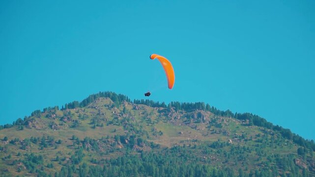 Tourist paragliding on parachute in blue sky background and the mountain at Manali in Himachal Pradesh, India. Adventure activity in Manali. Tourist activity during Summer holidays.