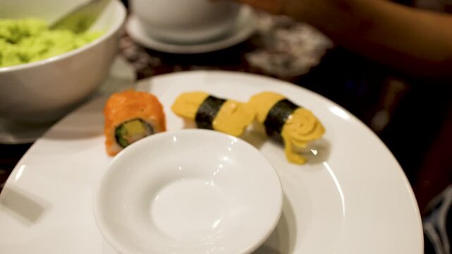 Person Preparing Wasabi and Sushi on White Plate at Asian Buffet