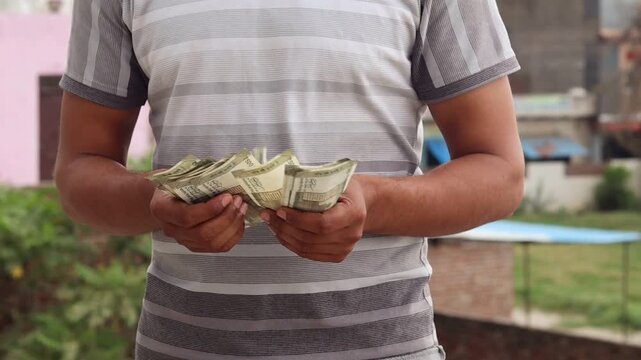 Close up of an Indian man counting five hundred rupee notes outdoors, male hands holding and counting Indian currency cash, finance and investment concept
