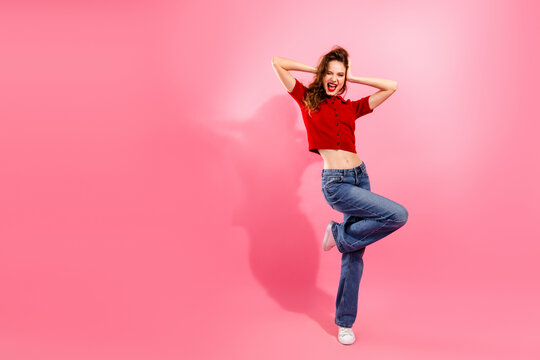 Cheerful young woman in red crop top jeans dancing on pink background for fashion lifestyle advertising