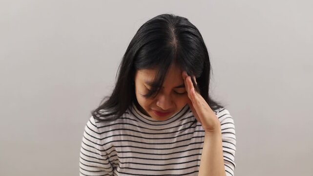 Depressed Asian woman sitting alone while covering face with hands in despair