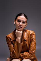 Obraz premium Stylish young woman exudes confidence in leather coat and glasses in studio setting