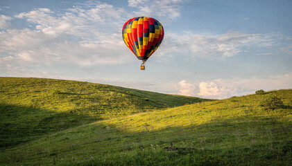 Fototapeta premium Colorful hot air balloon soar over vibrant green hills, summer sky backdrop