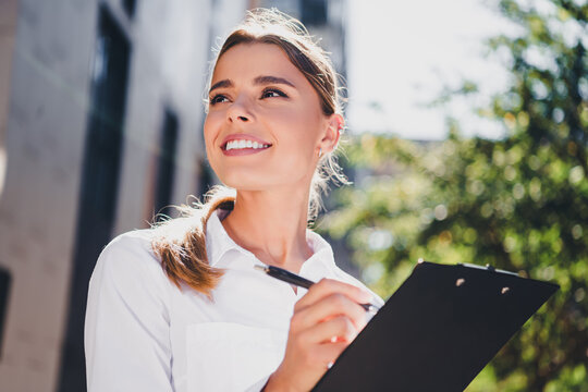 Smiling business woman holding clipboard outdoors taking notes &mdash; confident young professional conducting survey or inspection in urban setting