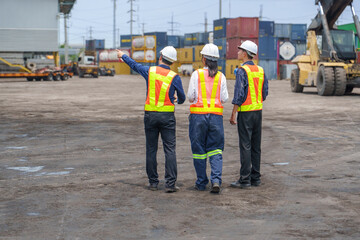 Logistics Managers in Safety Vests Walking Through Industrial Container Yard Toward Heavy Machinery in Asia © kudosstudio