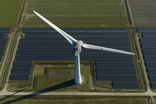 Aerial view of a large wind turbine standing amidst rows of solar panels in a renewable energy park surrounded by green fields Creil, Flevoland, Netherlands.
