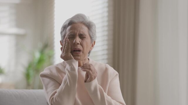 Senior woman feels intense headache pain touching face with hand experiencing deep stress severe toothache jaw discomfort poor elderly health sadness indoors