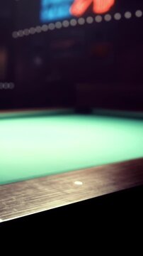 People gather around a green felt pool table at a bar. They focus on a game of pool and enjoy drinks. The lights illuminate the area, creating a lively atmosphere at night.
