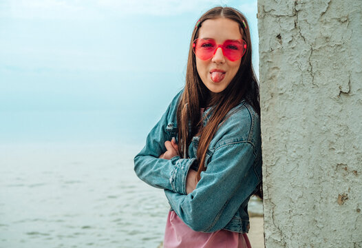 Carefree girl in sunglasses sticking her tongue out by the sea
