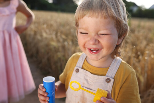 Laughing child playing with bubble wand in wheat field at golden hour