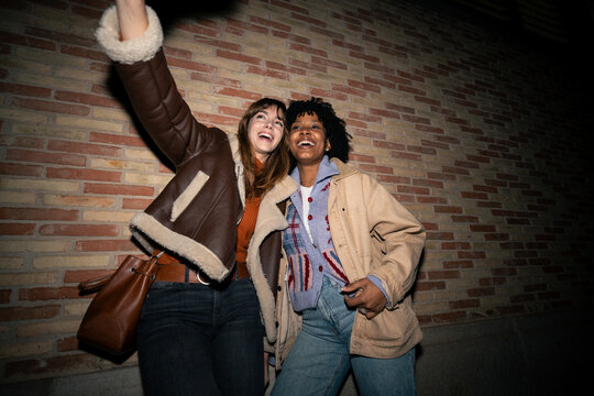 Smiling friends taking a selfie against a brick wall at night