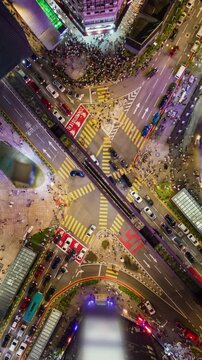 Top-down aerial timelapse of a busy intersection in Bukit Bintang, Kuala Lumpur. Crowds crossing streets, moving traffic and colorful city lights create dynamic urban nightlife and motion.