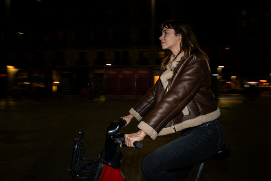 Woman cycling a bicycle through the city streets at night