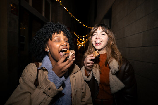 Friends eating dessert and laughing on city street at night