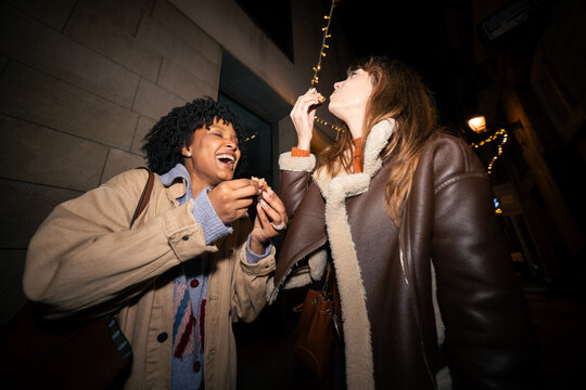 Happy friends laughing and eating dessert outdoors at night