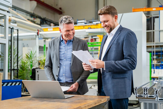 Smiling managers discussing production plans with laptop in factory
