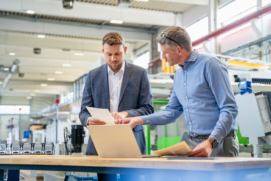 Manager and engineer discussing document with laptop in factory