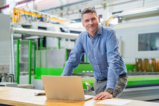 Satisfied manager with laptop standing in production hall