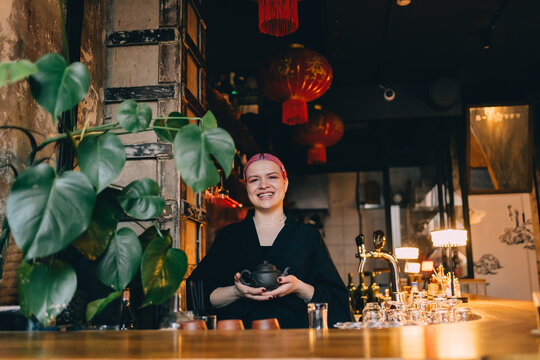 Smiling bartender holding a teapot behind the bar counter