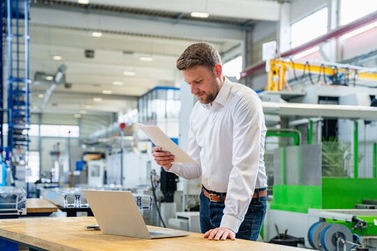 Manager reviewing documents by laptop in production hall