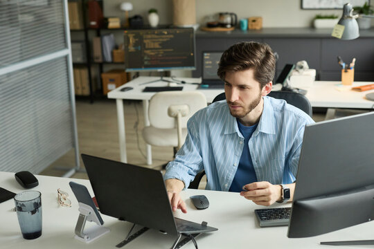 Professional developer coding on laptop at office workstation