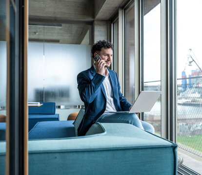 Smiling businessman making a call in modern office with a notebook